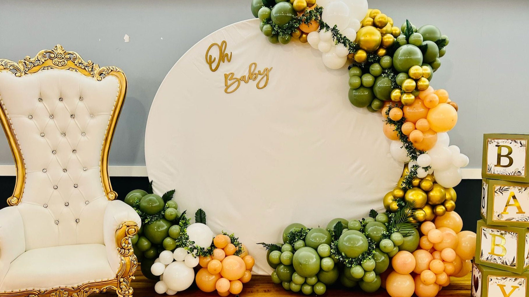 Decorative baby shower setup with balloons, a chair, and 'Oh Baby' sign.